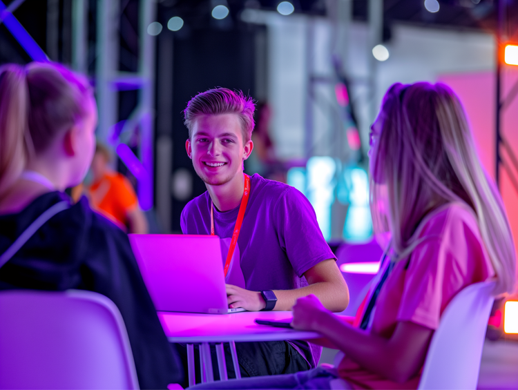 Three people at conference working on laptops with neon pink and purple background lighting