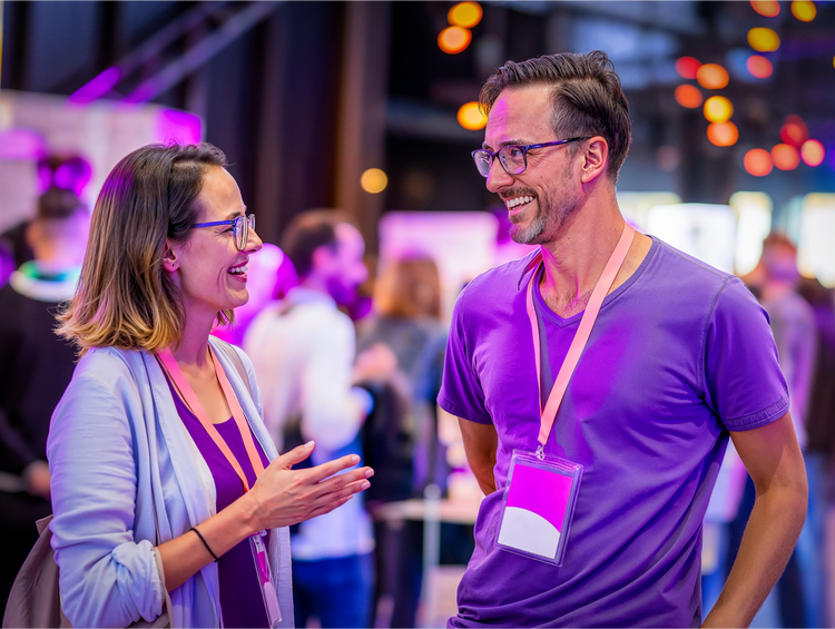 Two professionals wearing lanyards having a conversation at a conference with purple lighting