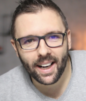 Barbudo com óculos sorrindo em camiseta cinza