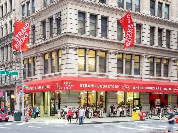 Exterior da Livraria Strand com toldos vermelhos e pessoas passando em frente à vitrine